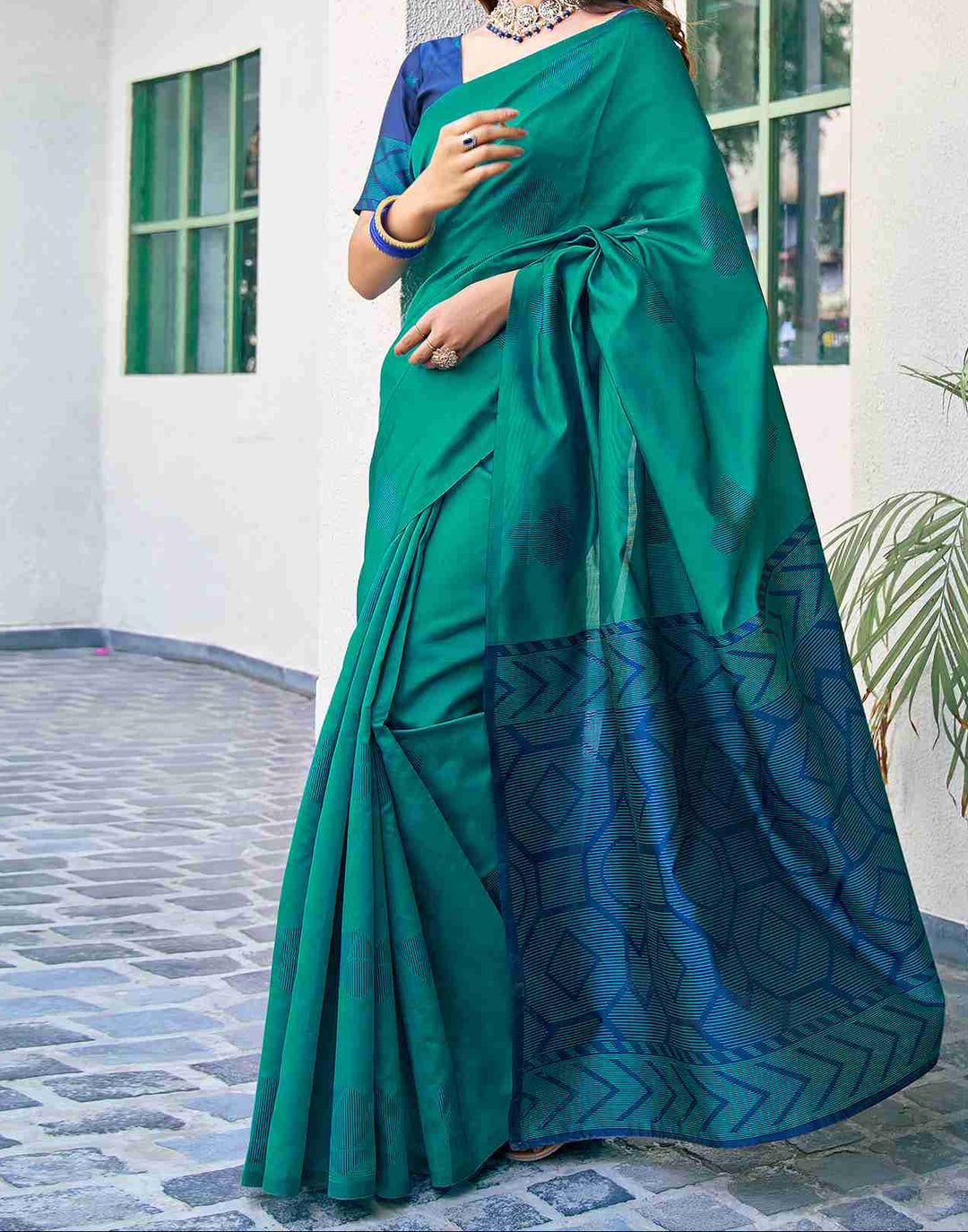 Full front view of model in teal green soft silk saree with navy blue chevron zari border and matching navy blouse