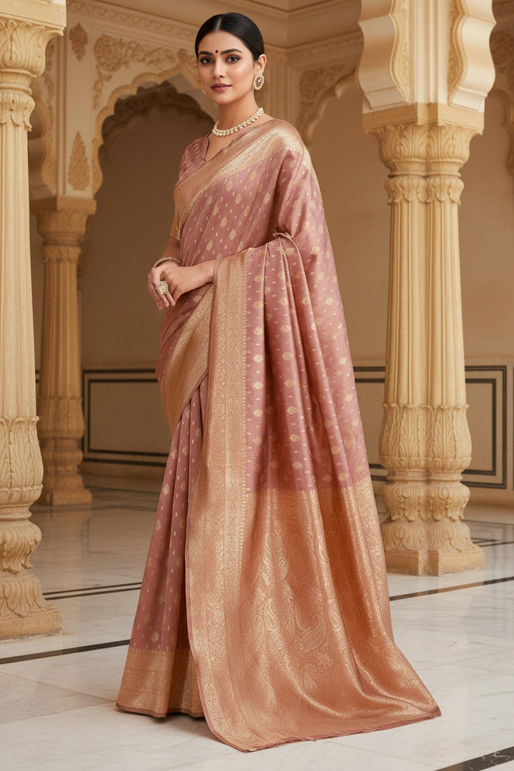 Three-quarter view of model in dusty rose Banarasi silk saree with antique gold zari buttas leaning against pillar outdoors