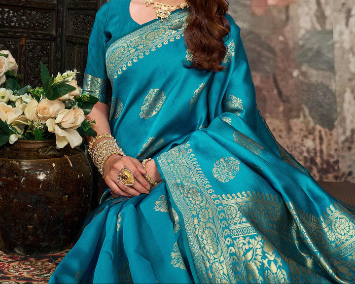 Seated close-up of model in cerulean blue Banarasi silk saree with gold temple necklace and bangles