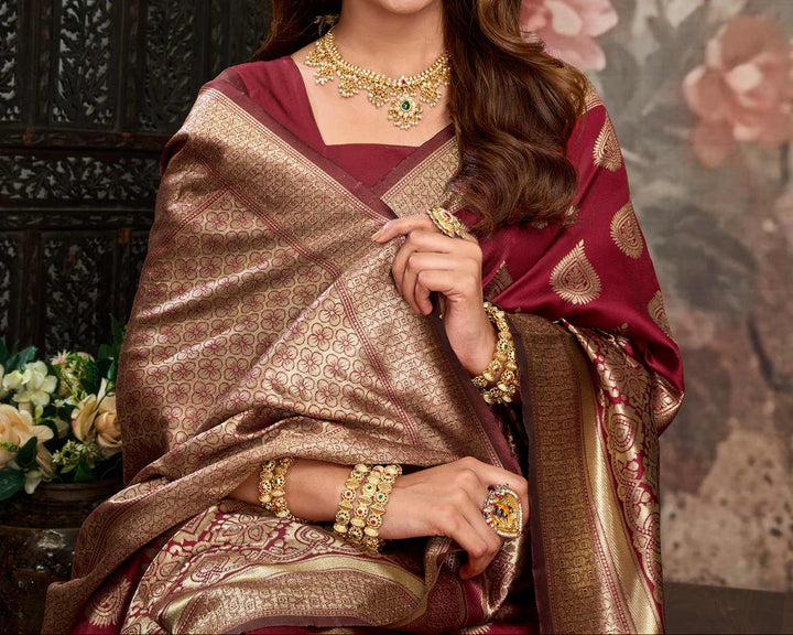 Seated close-up of model in maroon Banarasi silk saree with gold polki necklace, jhumkas, and gold bangles