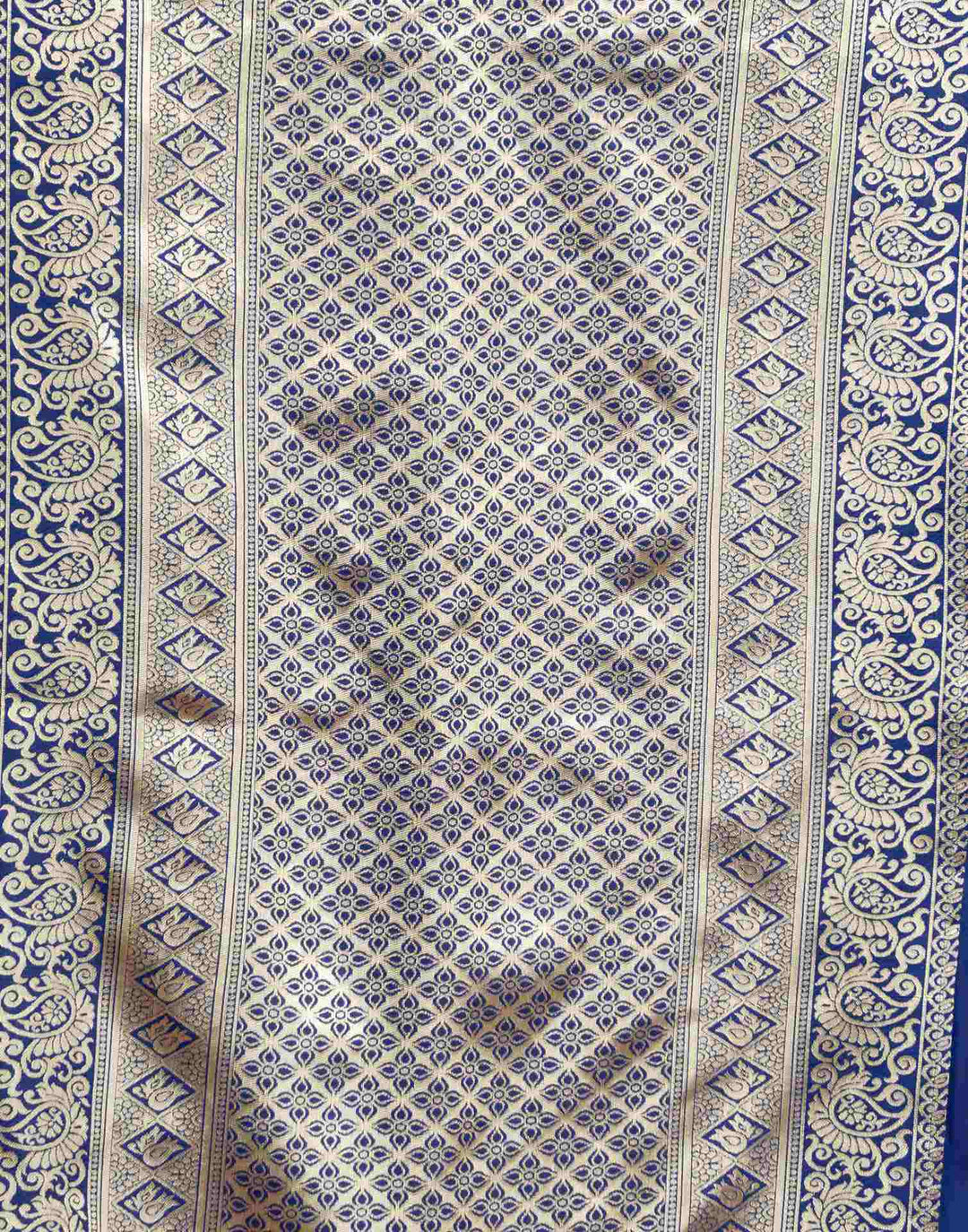 Close-up of royal blue Banarasi silk saree fabric showing dense gold zari jaal weave and paisley border