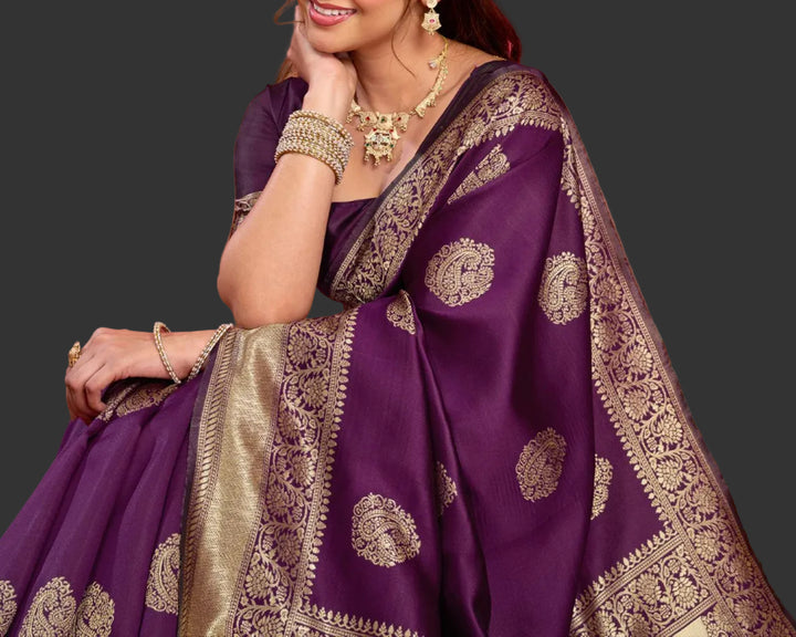Seated close-up of model in deep purple Banarasi silk saree with gold temple necklace and chandelier jhumkas