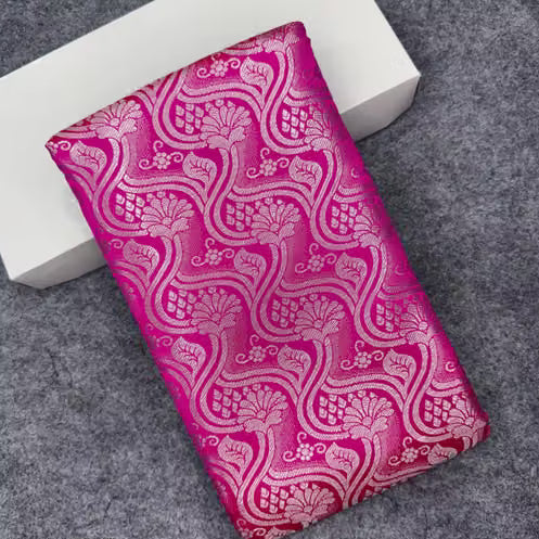 Folded flat lay of hot pink Banarasi silk saree showing all-over silver zari ogee wave jaal with floral and peacock motifs